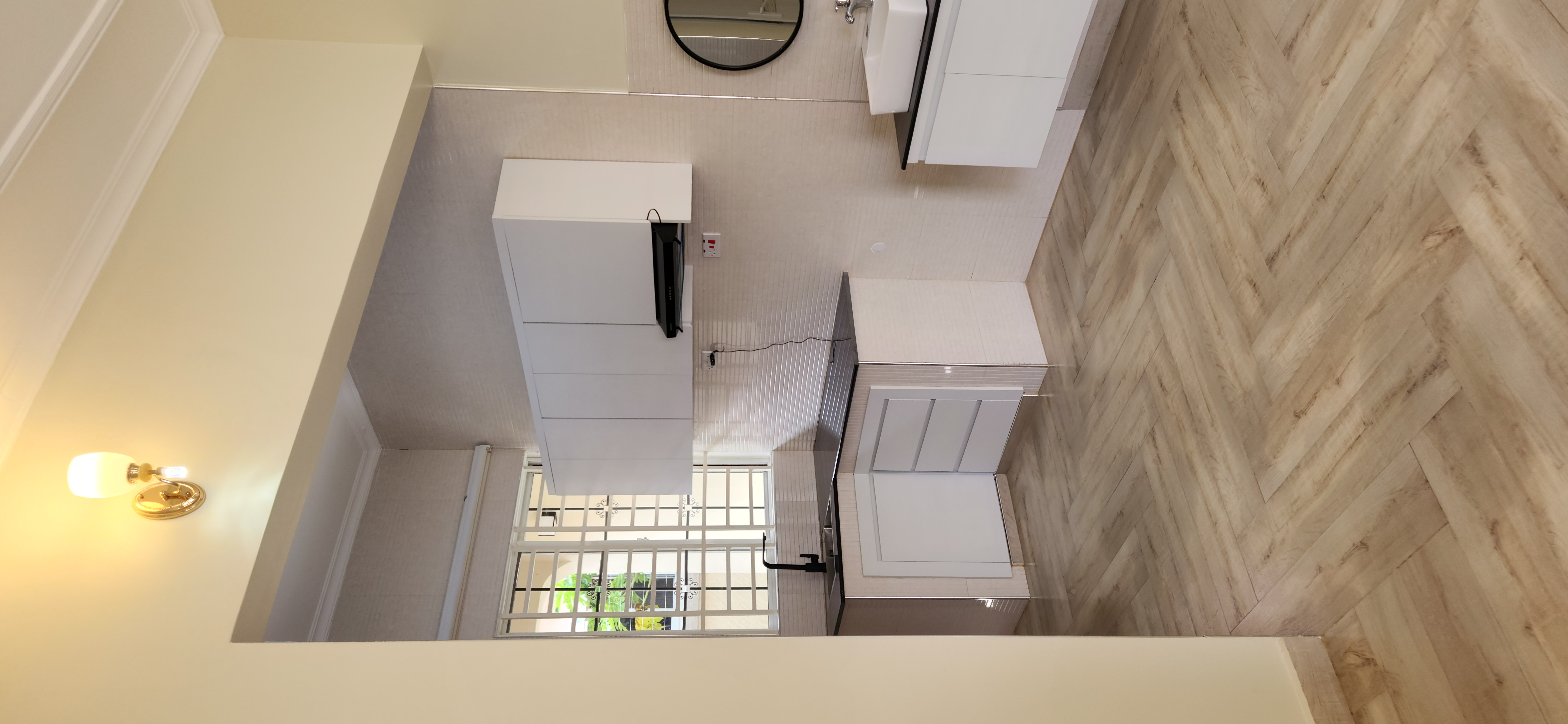 A clean, bright bathroom with timber flooring and a round mirror.